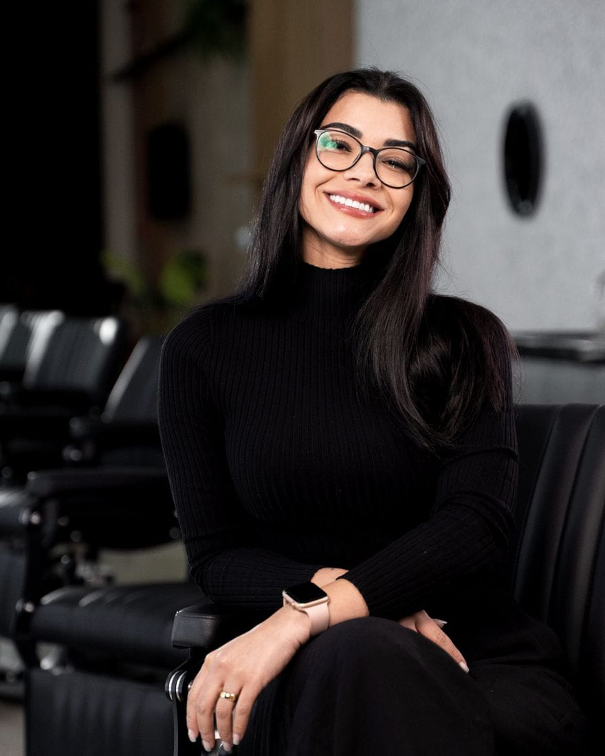 Jéssica Santos sentada na cadeira da sua barbearia, em ambiente de tons escuros.