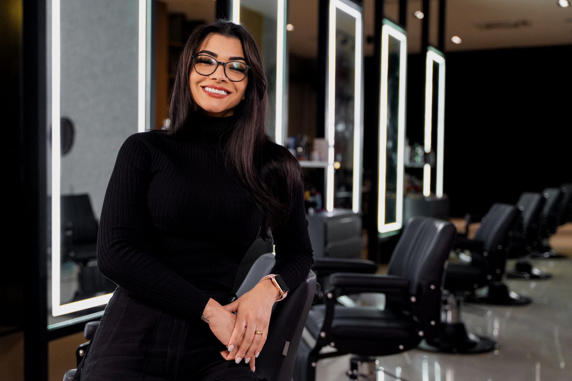 Jéssica Santos na barbearia, ao lado da cadeira de barbeiro, com o olhar voltado para a câmera.