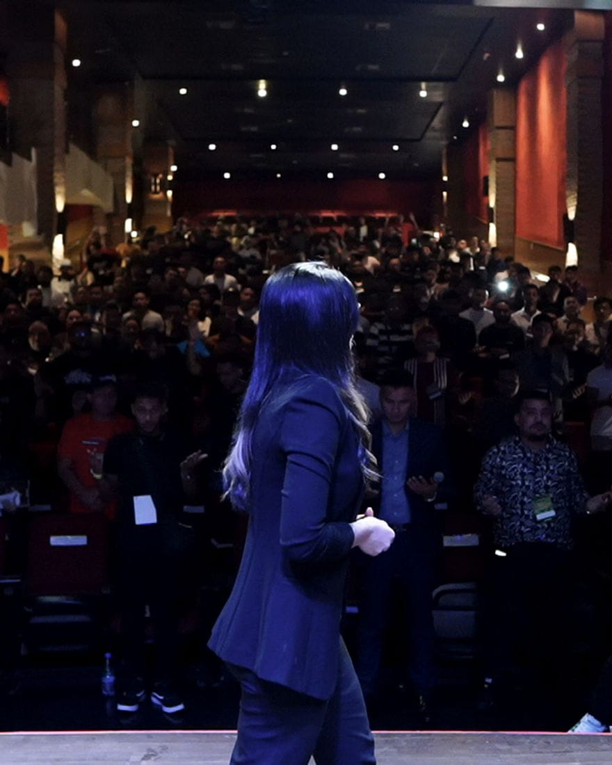 Jéssica Santos de costas, no palco, diante de uma plateia cheia de barbeiros.